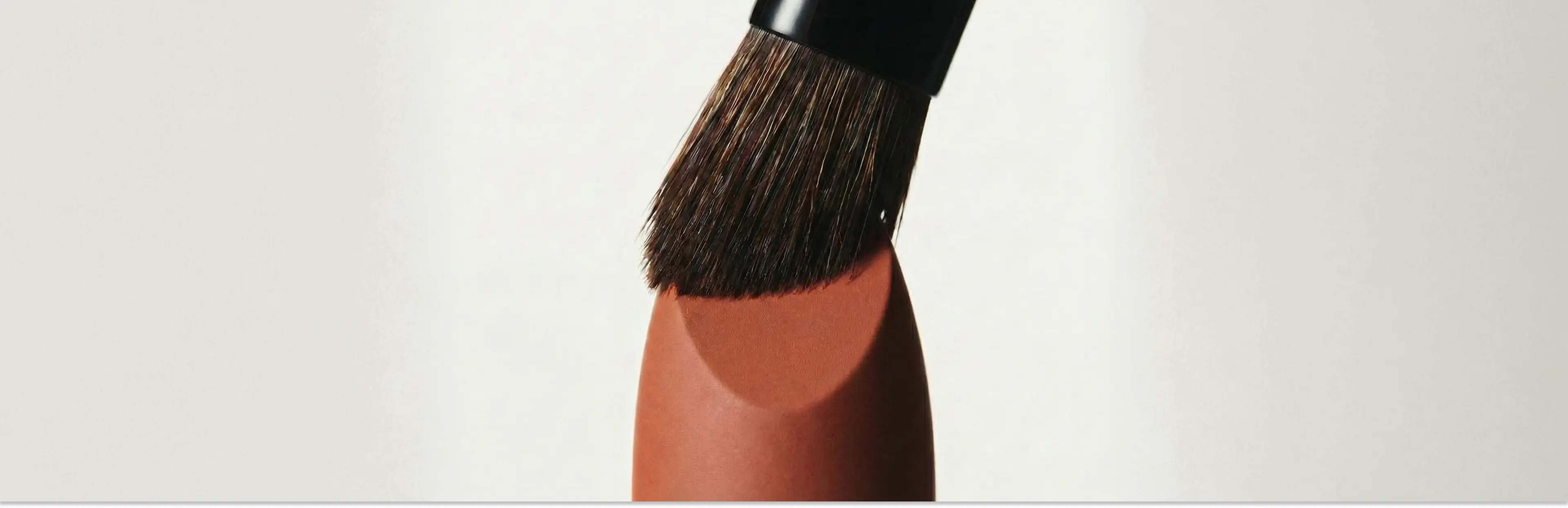 Makeup brush applying a swatch of makeup on a white background